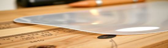 glossy HDPE material, shiny texture, bending slightly, photorealistic, on a wooden workbench, highly detailed, shadows and highlights, close-up shot, natural white, soft studio lighting, shot with a 100mm macro lens.