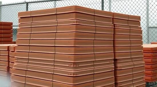 stacked polyethylene sheets, matte, arranged in a pyramid, photorealistic, outdoor storage facility with a chain-link fence backdrop, highly detailed, minor bends at corners, 24-70mm zoom lens, earthy brown, natural dim lighting